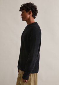 Ναυτικό πουλόβερ με μακριά μανίκια και στρογγυλή λαιμόκοψη, από υφασμάτινη υφή και χαλαρή εφαρμογή, συνδυασμένο με ανοιχτόχρωμο παντελόνι από κοτλέ.