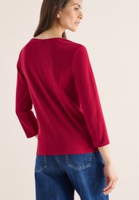 Czerwona longsleeve z okrągłym dekoltem, miękka tkanina i dopasowany krój, w połączeniu z niebieskimi dżinsami.