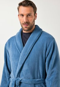 Tyrkysový župan z měkkého fleecu, s šálovým límcem, zavinovacím designem a zavazovacím páskem v oblasti pasu. Hladká textura s jemným leskem.