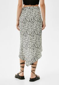 Mustat midi-hameet valkoisella kukkakuviolla, kevyttä materiaalia, epäsymmetrinen helma, yhdistetty mustien nyöri-sandaalien ja lyhyen topin kanssa.