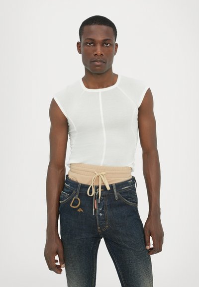 White sleeveless top with a fitted design, paired with dark blue jeans featuring gold stitching, a beige waistband, and a decorative D-shaped hardware accent.
