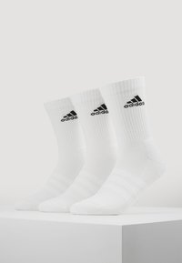 Valged sportlikud sokid ribakujulise tekstuuriga, millel on must Adidas'i logo ja kolm triibulikku aksenti varre peal. Kuvatud on kolm paari.