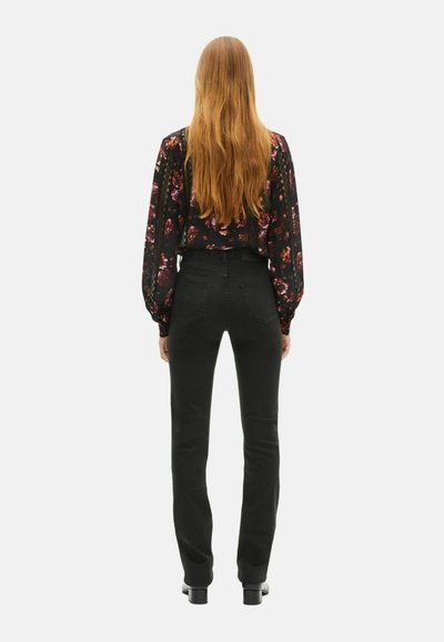 Jeans negros de tiro alto con un diseño ajustado, combinados con una blusa negra de manga larga con estampado floral, vistos desde la parte trasera.