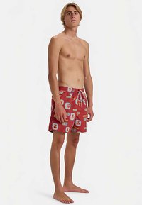 Punaiset uimashortsit, joissa on monivärisiä kuvioita, joustava vyötärönauha ja kiristysnyöri. Kevyt materiaali, polven pituinen leikkaus.