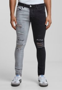 Jeans ajustados con un diseño de bloques de colores, un lado gris y el otro negro. Presenta áreas desgastadas y el texto bordado "Sr. Cuchillo".