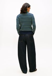 Πλεκτό μπλε πουλόβερ με πράσινες και λευκές ρίγες, με ριμπ λαιμόκοψη και μανσέτες. Συνδυασμένο με ευρύχωλο τζιν παντελόνι σκούρου χρώματος με πίσω τσέπες.