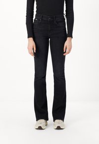 Black flared jeans with a high waist, made of denim. Features two front pockets, and subtle stitching details, styled with beige sneakers.