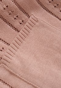 Rosa strikket stoff med et teksturert mønster som har små åpne masker, en ribbestrikket krage og glatte områder for ekstra detaljer.