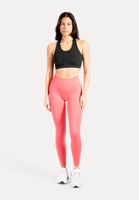 Schwarzer Sport-BH, hoch taillierte pinke Leggings und weiße Sportschuhe. Glatte Textur, körperbetontes Design und kontrastreiche Farben.