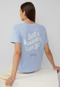 T-shirt en coton bleu clair avec des manches courtes, arborant un texte blanc au dos : "PASSEZ UNE MERVEILLEUSE JOURNÉE PAISIBLE" et un texte plus petit en noir en dessous.