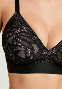 Zwarte kanten bralette met een bloemendessin, V-vormige halslijn en een stevige zwarte band voor ondersteuning. Zachte textuur met verstelbare bandjes.