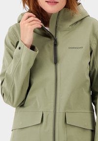 Grön vattentät jacka med passande huva, dragkedjeförslutning och stora framfickor. Har en slät textur och minimalistisk design.