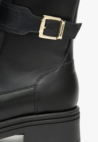 Stivale in pelle nera con fibbia decorativa, texture liscia, cuciture ben definite e un tacco solido con una base piattaforma a contrasto.