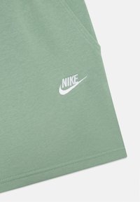Vihreät puuvillashortsit, joissa on sileä pinta, ja alhaalla vasemmalla valkoinen Nike-logo brodeerattuna. Mukana sivutasku.