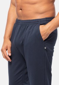 Marineblauwe sportieve joggers van zachte stof, met een elastische tailleband, zijzakken en een klein logo-accent op de bovenbeen.