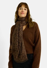 Bufanda marrón con estampado, hecha de tela suave, con diseño de estampado de leopardo y bordes deshilachados, colocada alrededor del cuello.