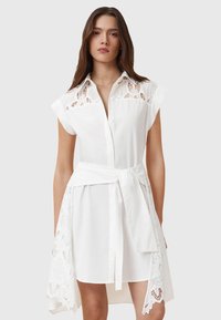 Weißes Hemdkleid mit kurzen Ärmeln, Spitzenakzenten an den Schultern, einem taillierten Bund und einem asymmetrischen Saum mit Spitzenbesatz.