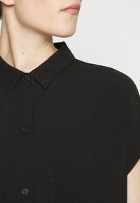Black collared shirt with short sleeves, front button closure, and a chest pocket. Smooth texture with a minimalist design.