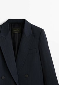 Blazer bleu marine foncé avec fines rayures, larges revers, boutons croisés et une poche poitrine, présenté sur fond blanc.
