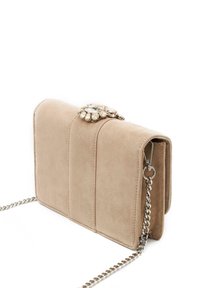 Bolso cruzado de ante beige con cadena plateada, que presenta un cierre con joyas y tres paneles acolchados verticales.