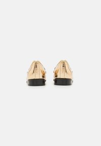 Chaussures métalliques dorées avec une texture lisse et un design à bout pointu, dotées de talons noirs et d'une finition brillante sur le matériau supérieur.