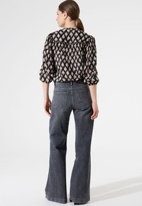 Schwarz-und-tan gemusterte Bluse mit Puffärmeln, kombiniert mit dunkelgrauen Schlagjeans. Sichtbare Rückendetails und strukturierte Passform.