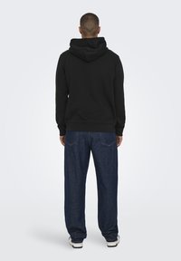 Felpa nera con cappuccio dalla vestibilità rilassata, abbinata a jeans in denim blu morbidi e larghi. Il tessuto sembra morbido, con polsini e orlo a coste.