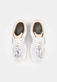 White Nike Air sneakers with light gray accents, featuring perforated toe box, flat laces, and a cushioned, beige insole.