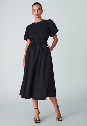 Črna midi obleka s puhastimi rokavi, elastiko na pasu in stranskimi žepi. Gladek material; sproščen dizajn z tekočo silhueto.