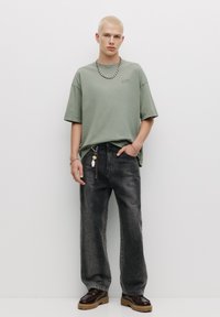 Tricou verde supradimensionat din bumbac, blugi negri decolorati, pantofi masivi maro cu șireturi, lănțișor de argint, stil casual de stradă.