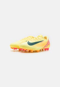 Botas de fútbol amarillas con parte superior texturizada, swoosh verde y suela salpicada de colores en tonos naranjas y rosas.