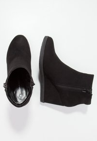 Bottines à talons compensés noires en matériau ressemblant à du suède. Elles disposent d'une fermeture zippée sur le côté, d'une texture lisse et d'un design à bout rond.