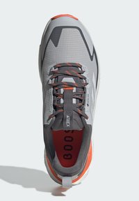 Szare buty sportowe z teksturowaną cholewką, pomarańczowymi akcentami i grubą białą podeszwą. Posiada elastyczne sznurówki i uchwyt na pięcie.