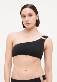 Čierny bikiny top s jedným ramienkom vyrobený z hladkého materiálu, so zúženým akcentom a strieborným kovovým zdobením na ramienku.