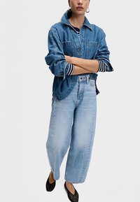 Jeansskjorta med krage, två bröstfickor och uppvikta ärmslut; kombinerad med ljusblå, vida jeans. Svarta, perforerade slip-ons.