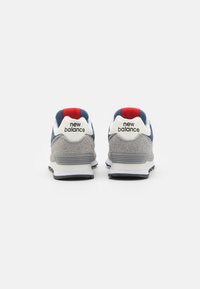 Zapatillas deportivas de ante gris y textil con acentos en azul marino y una lengüeta roja; presentan un logo blanco y una suela de goma negra.