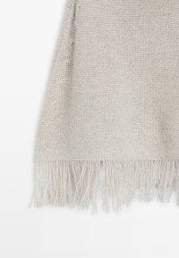 Plaid tricoté beige clair avec un motif texturé et une longue frange douce le long du bord. Convient pour superposer ou pour une utilisation décorative.