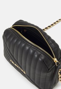 Svart läderväska med kviltad yta och guldfärgade detaljer, med dragkedjestängning och kedjeaxelrem. Varumärket präglat på framsidan.