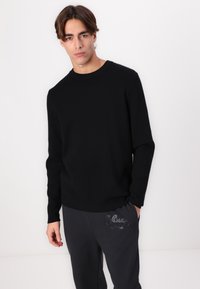 Black knit sweater with a crew neck, long sleeves, and a relaxed fit, paired with gray sweatpants featuring a subtle logo detail.
