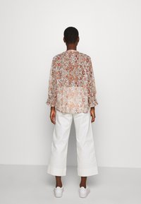 Blusa floral ligera y transparente en tonos cálidos, con mangas fruncidas y un corte holgado, combinada con pantalones blancos de pierna ancha y zapatillas.