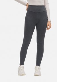 Leggings grises de talle alto hechos de un tejido texturizado, con un diseño ajustado y combinados con zapatillas deportivas blancas.