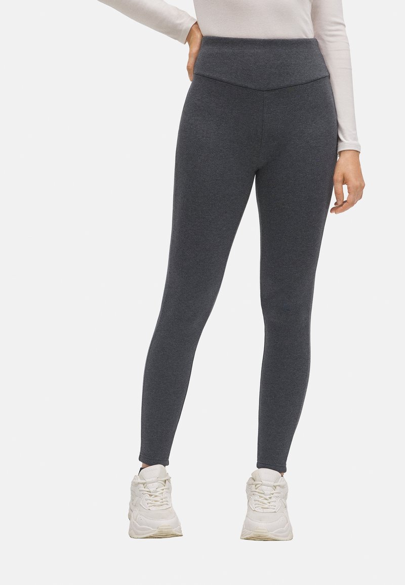 Leggings grises de talle alto hechos de un tejido texturizado, con un diseño ajustado y combinados con zapatillas deportivas blancas.