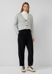 Cardigan tricoté gris clair avec un décolleté en V profond et trois boutons, associé à un pantalon noir ajusté et des baskets crème avec des lacets noirs.