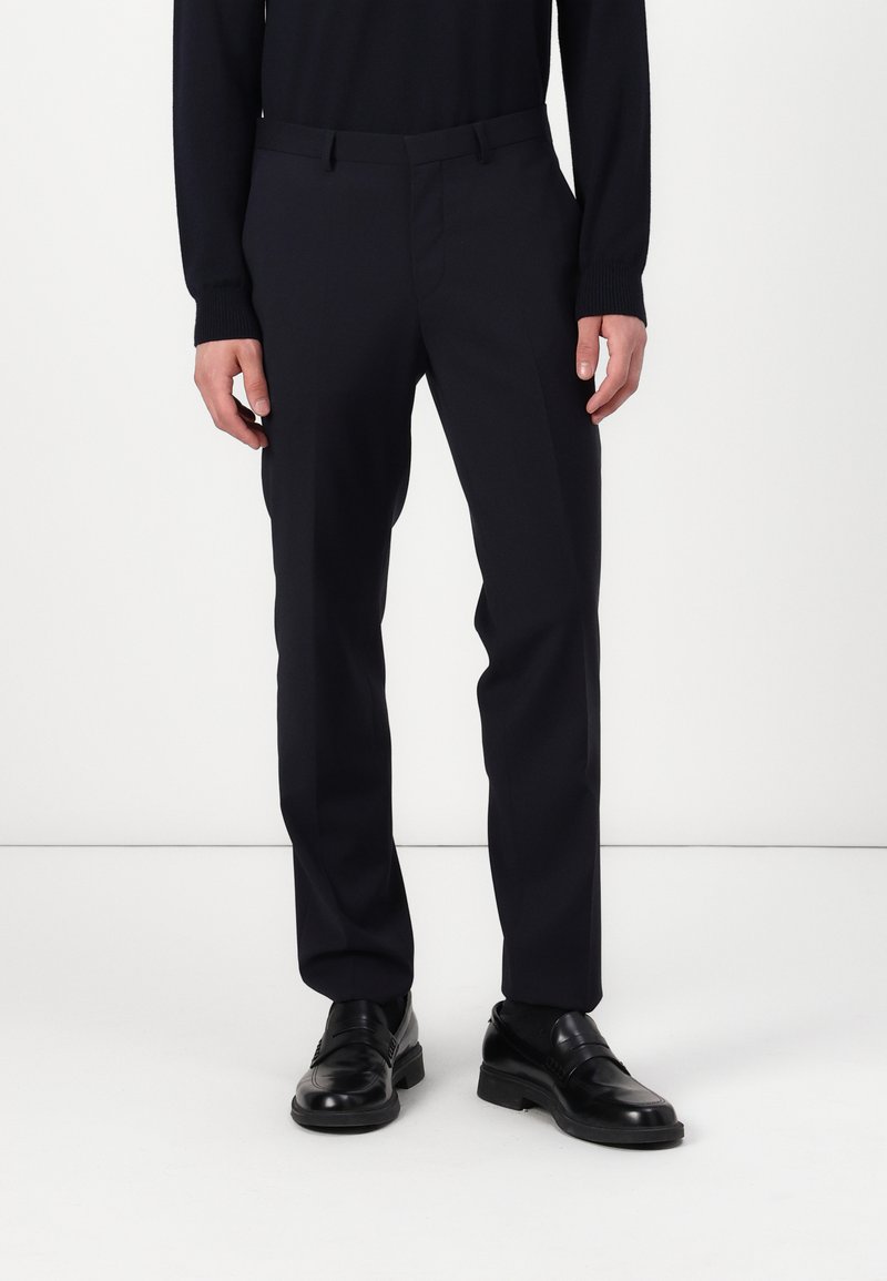 Navy dress trousers with a tailored fit, featuring a flat front, side pockets, and smooth fabric. Paired with black leather shoes.