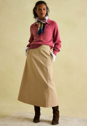 Rosa gestrickter Pullover mit Kragen, kombiniert mit einem beigen Maxirock mit seitlichen Taschen und braunen Wildlederschuhen bis zum Knie.