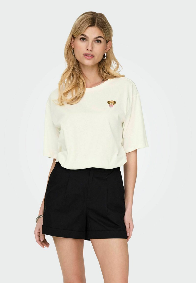 Crème korte mouw t-shirt met een hondenafbeelding op de borst en een losse pasvorm, gecombineerd met hoge zwarte shorts met plooien.