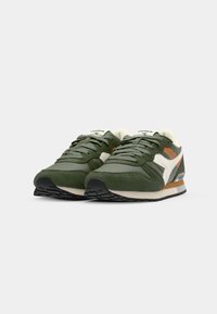Green athletic shoes with suede and mesh materials. Features white and brown accents, lace-up design, thick rubber sole, and textured surface.