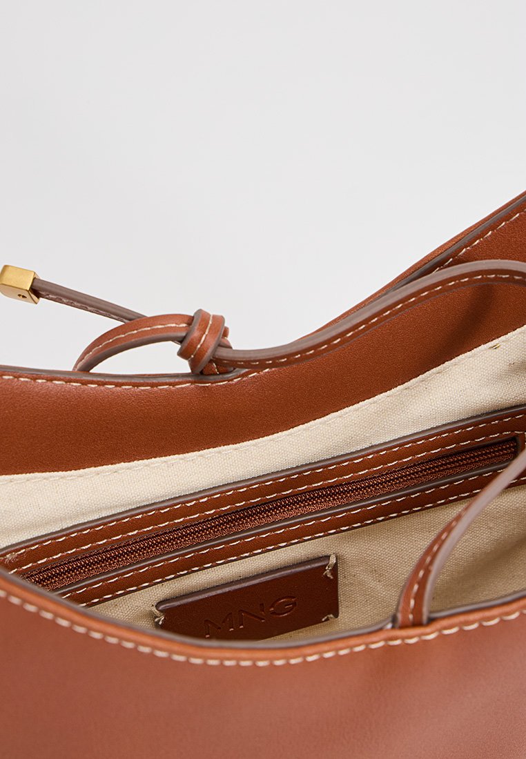 Braune Lederhandtasche mit glatter Textur, ausgestattet mit einer Reißverschlusstasche, beige Innenfutter und einem Logotag. Abgerundet mit tonal abgestimmtem Nähen.