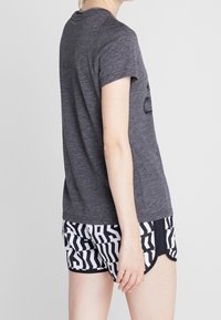 Grå kortærmet t-shirt med rund hals, parret med sort-hvide mønstrede shorts med geometriske designs og kanter.