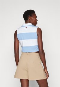 Camisa sin mangas tipo polo con rayas horizontales en azul y blanco, acompañada de pantalones cortos color beige claro con cinturón. Material de mezcla de algodón.